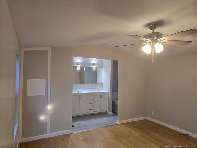 unfurnished bedroom with baseboards, ensuite bathroom, vaulted ceiling, light wood-type flooring, and a sink