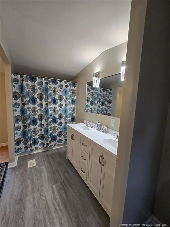 full bathroom featuring double vanity, vaulted ceiling, a sink, and wood finished floors