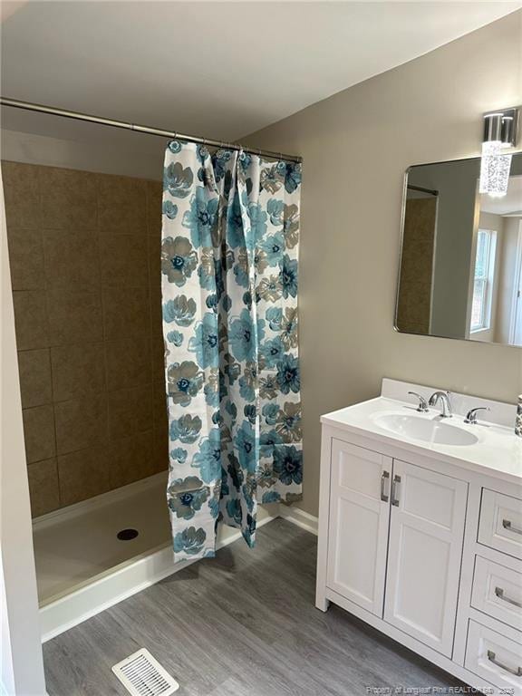 full bathroom featuring visible vents, a tile shower, vanity, and wood finished floors