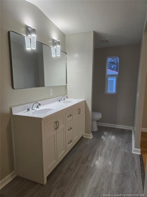 bathroom with double vanity, wood finished floors, a sink, and toilet