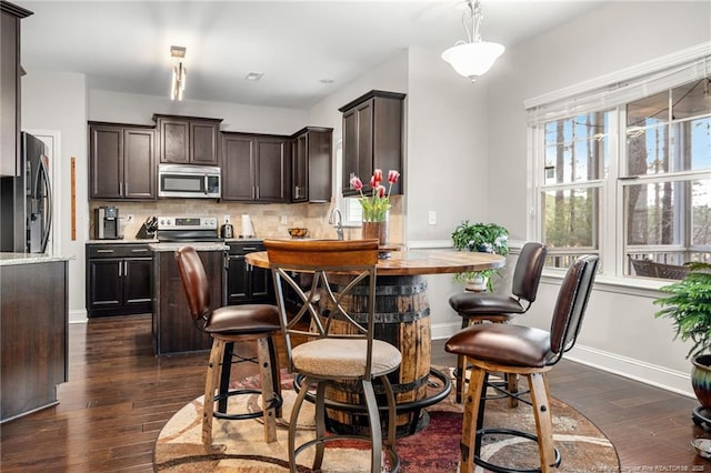 kitchen with dark brown cabinetry, tasteful backsplash, appliances with stainless steel finishes, dark hardwood / wood-style floors, and pendant lighting