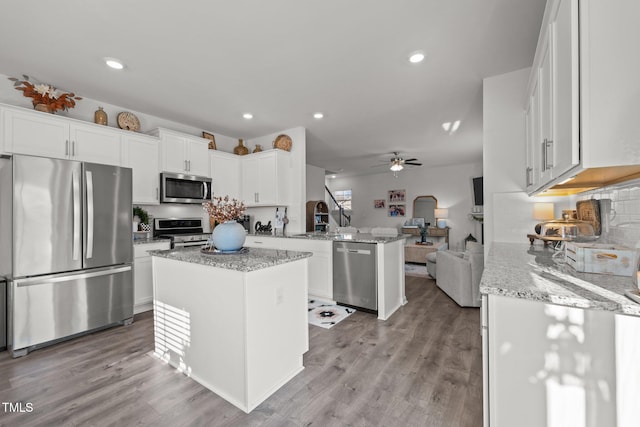 kitchen featuring a kitchen island, appliances with stainless steel finishes, white cabinets, light stone counters, and kitchen peninsula