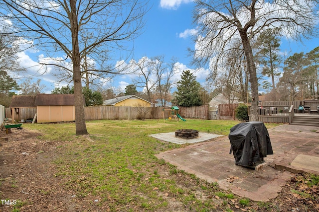 view of yard featuring a fenced backyard, a playground, a shed, a fire pit, and an outdoor structure