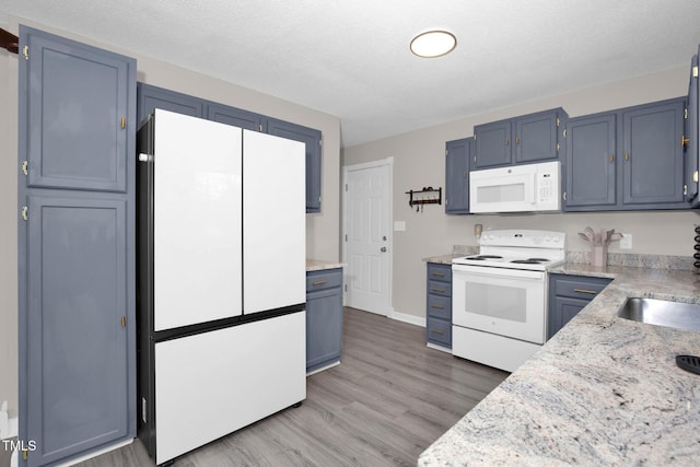 kitchen with blue cabinetry, white appliances, a textured ceiling, and light wood-type flooring