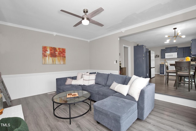 living area featuring a wainscoted wall, wood finished floors, crown molding, and ceiling fan with notable chandelier