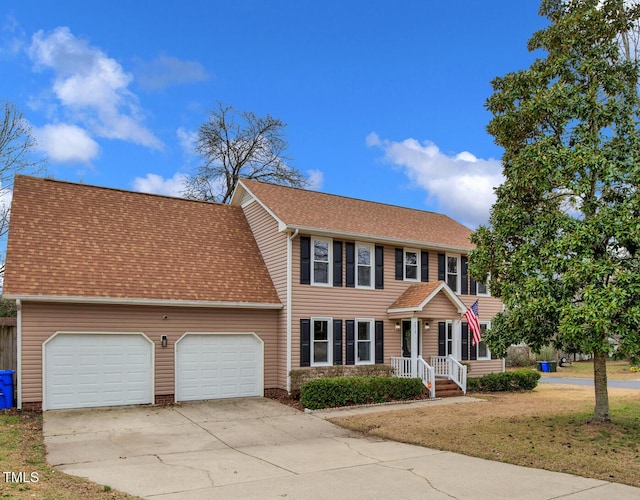 colonial inspired home with a front lawn, an attached garage, driveway, and roof with shingles