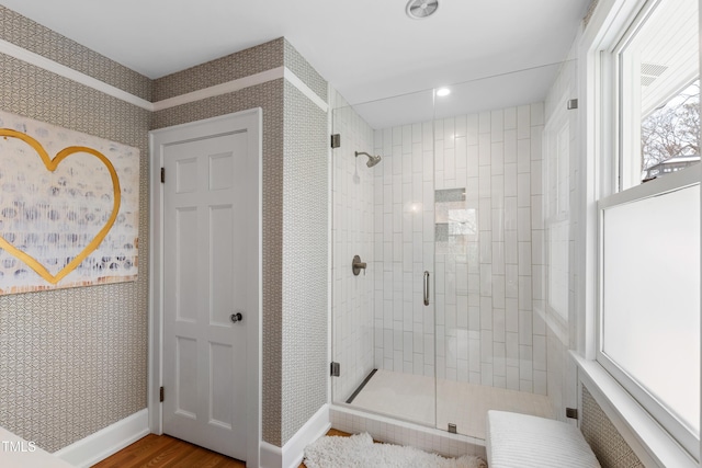 full bath with wallpapered walls, a shower stall, baseboards, and wood finished floors