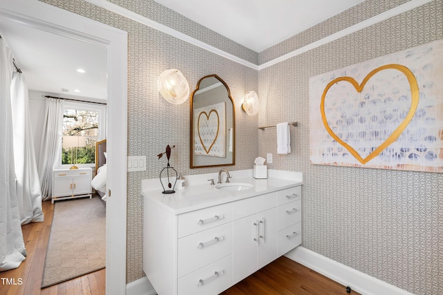 bathroom with wood finished floors, vanity, baseboards, and wallpapered walls