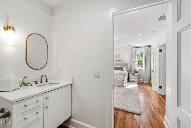 bathroom with crown molding, visible vents, vanity, wood finished floors, and baseboards