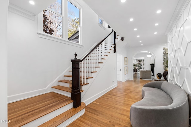 foyer featuring baseboards, arched walkways, crown molding, light wood-type flooring, and recessed lighting