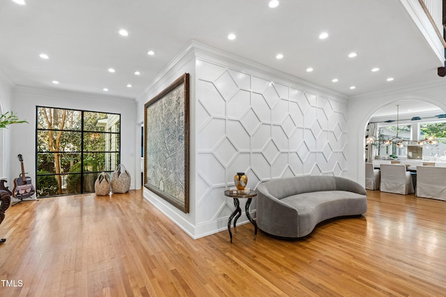 sitting room featuring light wood finished floors, an accent wall, ornamental molding, and arched walkways