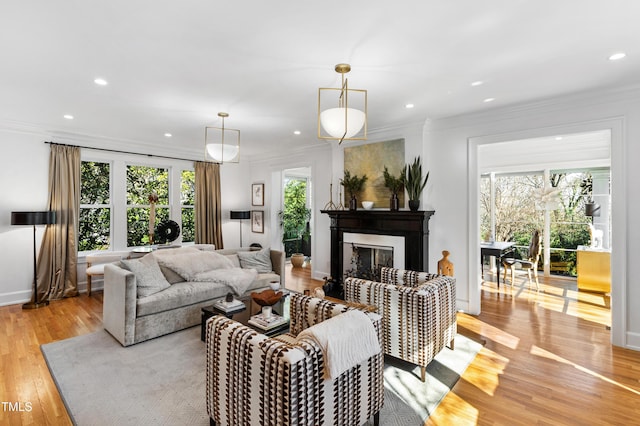 living area featuring recessed lighting, light wood-type flooring, a glass covered fireplace, and crown molding