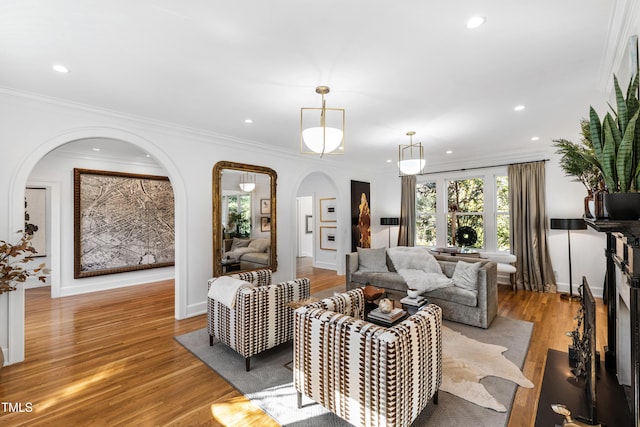 living room with arched walkways, baseboards, ornamental molding, light wood-style floors, and recessed lighting