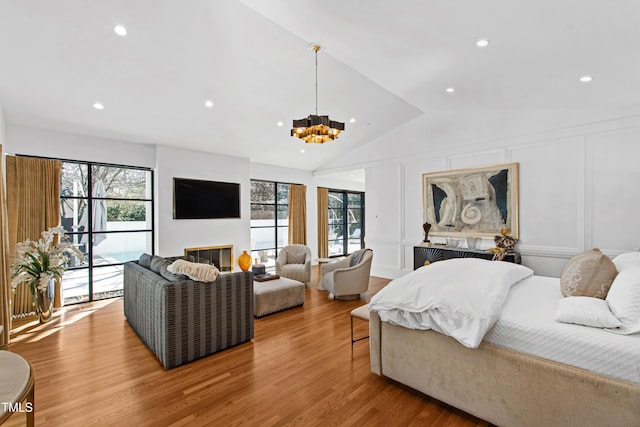 bedroom featuring recessed lighting, a decorative wall, a glass covered fireplace, vaulted ceiling, and wood finished floors