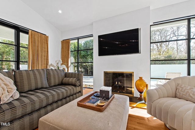 living area with a wealth of natural light, lofted ceiling, a glass covered fireplace, and wood finished floors