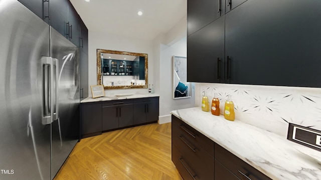 kitchen with modern cabinets, high end refrigerator, light stone counters, and recessed lighting