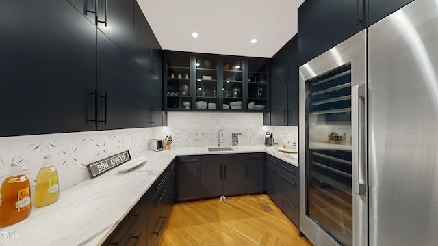 kitchen featuring glass insert cabinets, dark cabinetry, a sink, and built in refrigerator