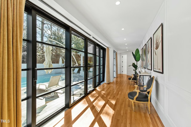 corridor featuring recessed lighting, a decorative wall, and light wood-style flooring