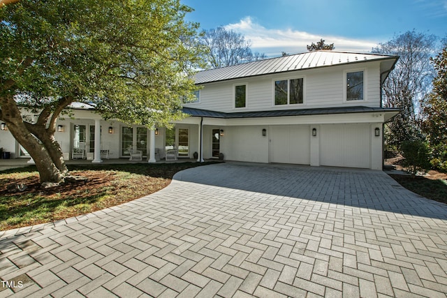 view of front of home with metal roof, an attached garage, a standing seam roof, covered porch, and decorative driveway