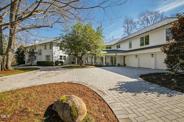 view of front of house featuring a standing seam roof, a chimney, metal roof, and decorative driveway