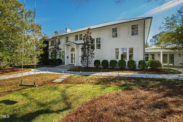 view of front of property featuring a chimney, metal roof, and a front yard