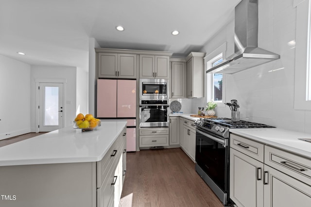 kitchen featuring dark wood-type flooring, stainless steel appliances, tasteful backsplash, and wall chimney range hood