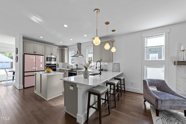 kitchen with sink, decorative light fixtures, appliances with stainless steel finishes, kitchen peninsula, and wall chimney range hood