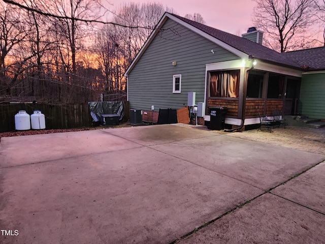 view of home's exterior with concrete driveway, a chimney, and a sunroom