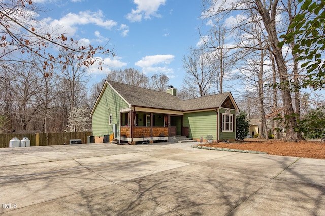 view of front facade featuring roof with shingles, concrete driveway, a chimney, and fence