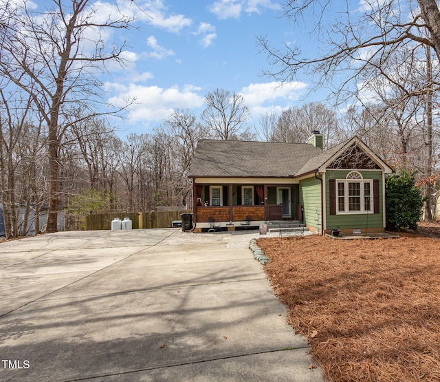 view of front of property with a porch, fence, concrete driveway, a shingled roof, and a chimney