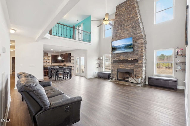 living room featuring a ceiling fan, baseboards, wood finished floors, and a stone fireplace