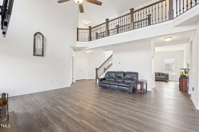 living room with ceiling fan, wood finished floors, a towering ceiling, baseboards, and stairs