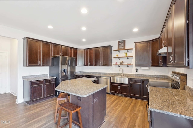 kitchen with stainless steel appliances, light wood-style flooring, a sink, dark brown cabinetry, and under cabinet range hood