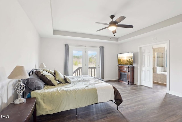 bedroom featuring access to exterior, baseboards, a tray ceiling, and wood finished floors