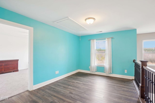 unfurnished room featuring a healthy amount of sunlight, attic access, visible vents, and dark wood-type flooring