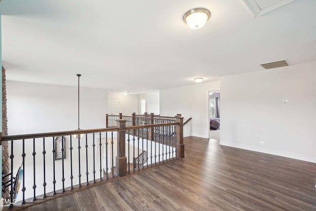 corridor featuring wood finished floors, visible vents, an upstairs landing, baseboards, and attic access