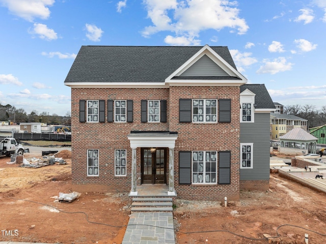 view of front facade featuring french doors, a shingled roof, and brick siding