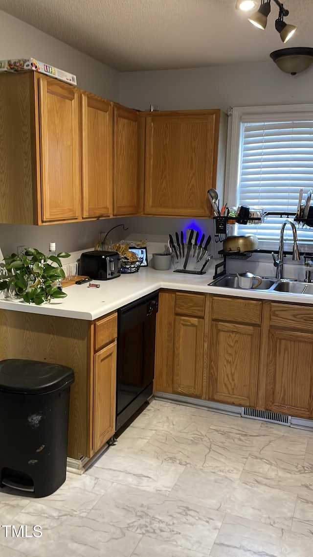 kitchen featuring marble finish floor, light countertops, black dishwasher, a sink, and brown cabinets