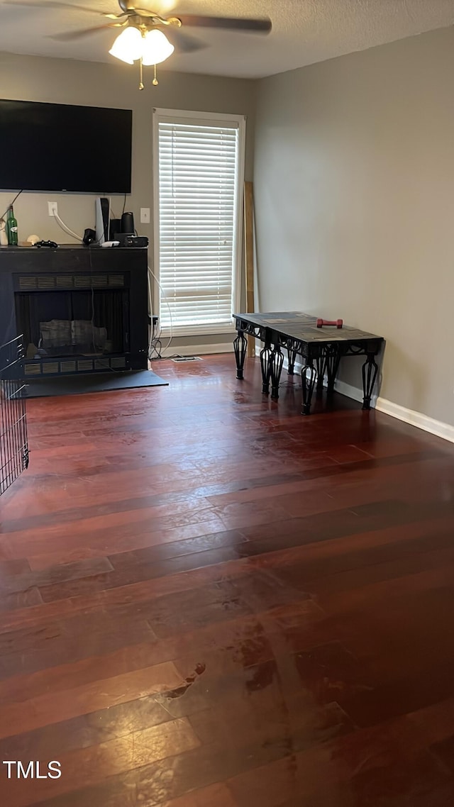 dining area with ceiling fan, baseboards, dark wood-style flooring, a textured ceiling, and a fireplace