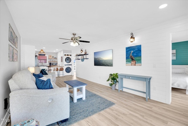 living room with light wood-type flooring, ceiling fan, and stacked washer and clothes dryer