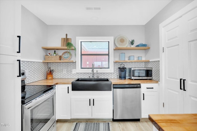 kitchen featuring white cabinetry, sink, stainless steel appliances, and butcher block countertops