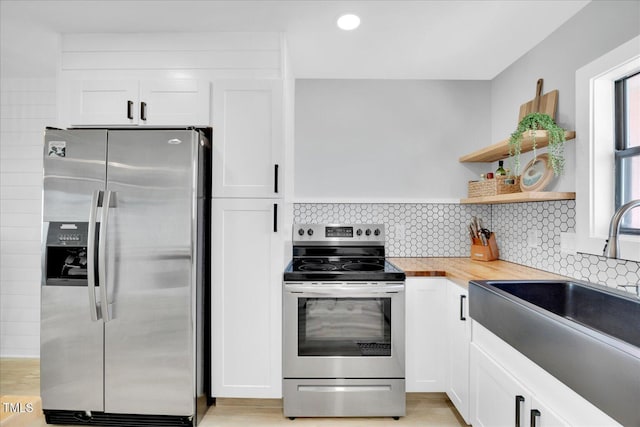 kitchen featuring stainless steel appliances, butcher block countertops, sink, backsplash, and white cabinets