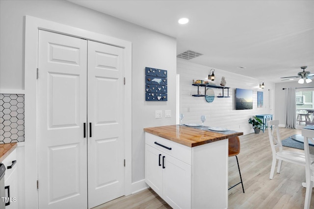 kitchen with butcher block counters, light wood-type flooring, kitchen peninsula, white cabinets, and a breakfast bar area