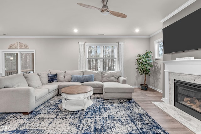 living room featuring a fireplace, light wood-style flooring, ornamental molding, ceiling fan, and baseboards