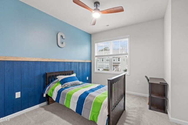 bedroom with carpet, visible vents, a ceiling fan, wood walls, and baseboards