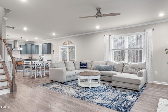 living area with light wood-style floors, stairs, visible vents, and ornamental molding