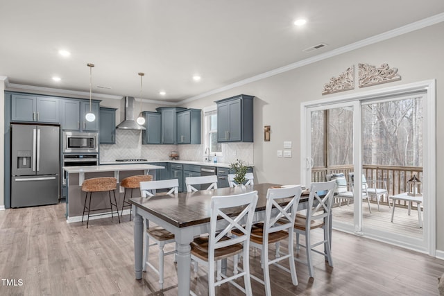 kitchen with stainless steel appliances, a kitchen island, light countertops, wall chimney range hood, and decorative light fixtures