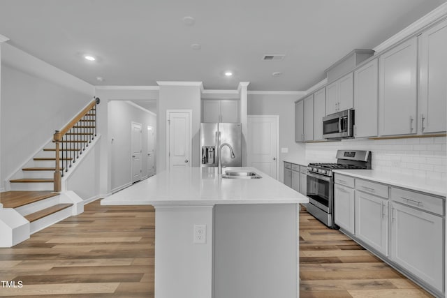 kitchen featuring a kitchen island with sink, light hardwood / wood-style flooring, sink, gray cabinets, and appliances with stainless steel finishes