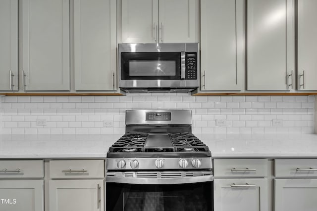 kitchen with appliances with stainless steel finishes, gray cabinetry, light stone countertops, and decorative backsplash