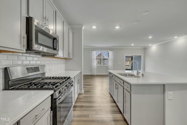 kitchen featuring sink, backsplash, crown molding, stainless steel appliances, and a kitchen island with sink